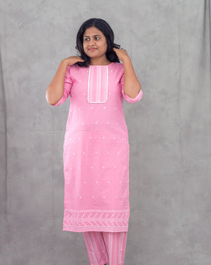 Woman wearing a pink traditional outfit with white patterns against a gray background