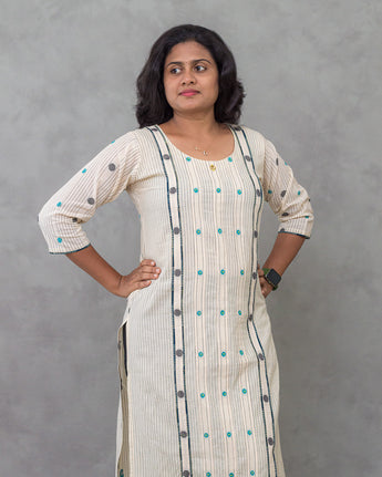 Woman wearing a long, light-colored dress with patterns against a gray background