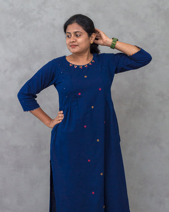 Person wearing a blue kurta with colorful buttons and pants on a gray background