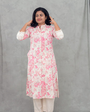 A women wearing a floral printed lace work pink color top with plain beige bottom on a grey background