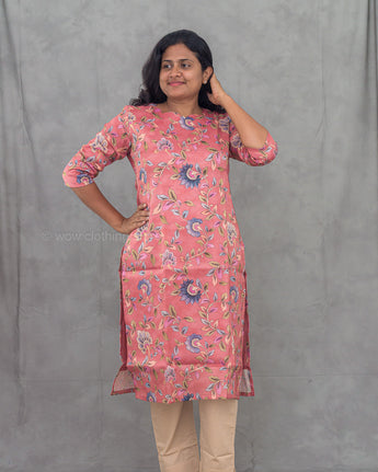 Woman wearing a pink floral kurti with beige pants against a gray background