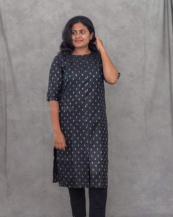 Woman wearing a black kurti with gold patterns against a gray background