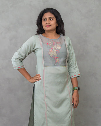 A lady wearing a plain top with elegant neck work linen kurti on a grey background