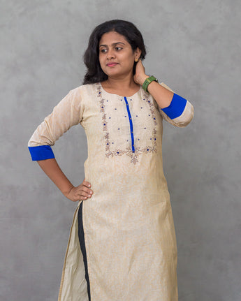 Woman wearing a cream kurta with blue accents against a gray background