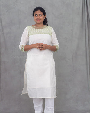 Woman wearing a white kurti with green embroidery against a gray background