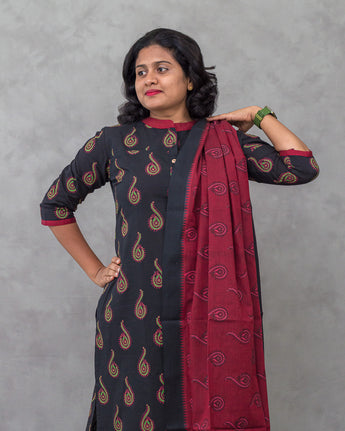 A women wearing printed black cotton kurti with plain bottom and printed maroon color dupatta on a grey background