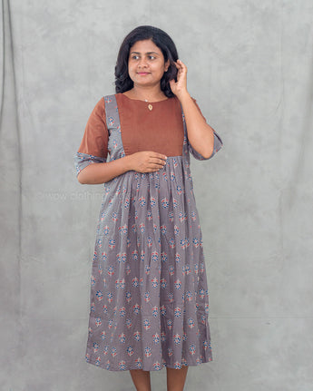Woman wearing a brown top and gray feeding dress with floral patterns against a gray background