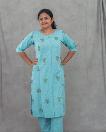 Woman wearing a light blue motif outfit with matching pants against a gray background