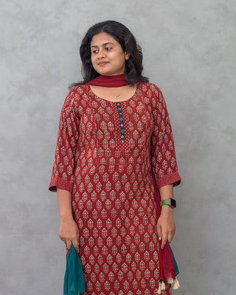 Woman wearing a maroon patterned kurti suit against a gray background