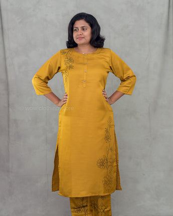 Woman wearing a mustard yellow kurta with floral embroidery against a gray background