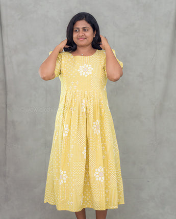 Woman wearing a yellow maternity dress with white floral patterns against a gray background