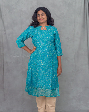 Woman wearing a blue floral kurti with beige pants against a gray background