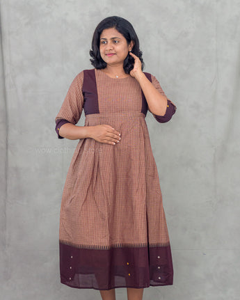 Woman wearing a brown and purple striped maternity dress against a gray background