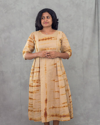 Woman wearing a beige and brown tie-dye dress against a gray background