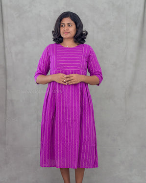 Woman wearing a purple maternity dress with zigzag patterns against a gray background