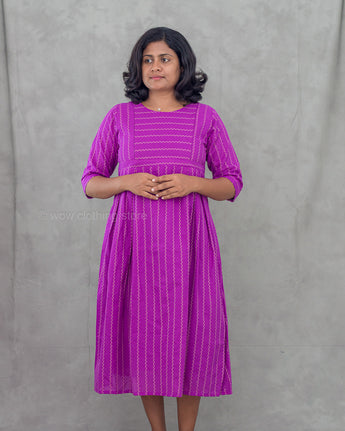 Woman wearing a purple maternity dress with zigzag patterns against a gray background