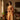 Woman in an orange saree standing in a room with decor elements.