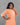 Woman wearing an orange kurta with white patterns against a gray background