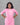 Woman wearing a pink traditional outfit with white patterns against a gray background