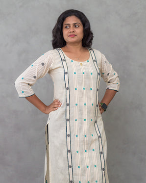 Woman wearing a long, light-colored dress with patterns against a gray background