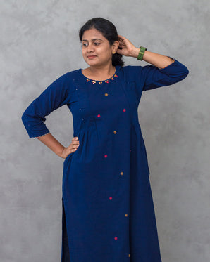 Person wearing a blue kurta with colorful buttons and pants on a gray background