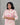 A women wearing a floral printed lace work pink color top with plain beige bottom on a grey background