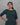 Woman wearing a dark green jacquard top against a gray background
