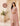 Woman in a pink traditional outfit standing in a decorative setting with flowers and architectural elements.
