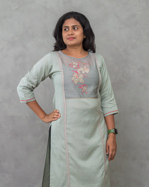A lady wearing a plain top with elegant neck work linen kurti on a grey background