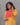 Woman wearing a yellow and orange traditional outfit against a gray background