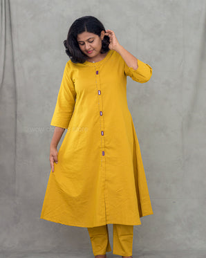 A women wearing a plain yellow kurti with mirror work and plain bottom on a grey background