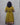 Person wearing a mustard yellow dress with black lace details on a gray background
