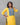 Woman wearing a yellow kurta with blue embroidery against a gray background