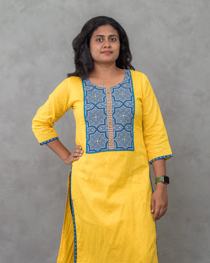 Woman wearing a yellow kurta with blue embroidery against a gray background