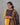 Woman wearing a yellow outfit with a patterned dark blue and orange dupatta against a gray background