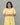 Woman wearing a yellow feeding dress with white floral patterns against a gray background