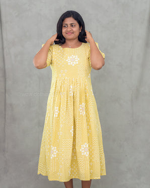 Woman wearing a yellow maternity dress with white floral patterns against a gray background