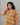 Woman wearing a mustard yellow and brown patterned dress against a gray background