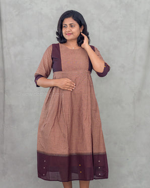 Woman wearing a brown and purple striped maternity dress against a gray background