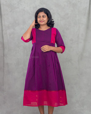 Woman wearing a purple and pink maternity dress against a gray background